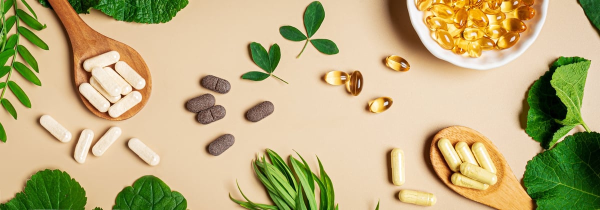 Plant based supplements. Organic vitamins. Homeopathy and alternative herbal medicine. Vegan capsules and pills, green plant leaves on beige background, top view, banner.