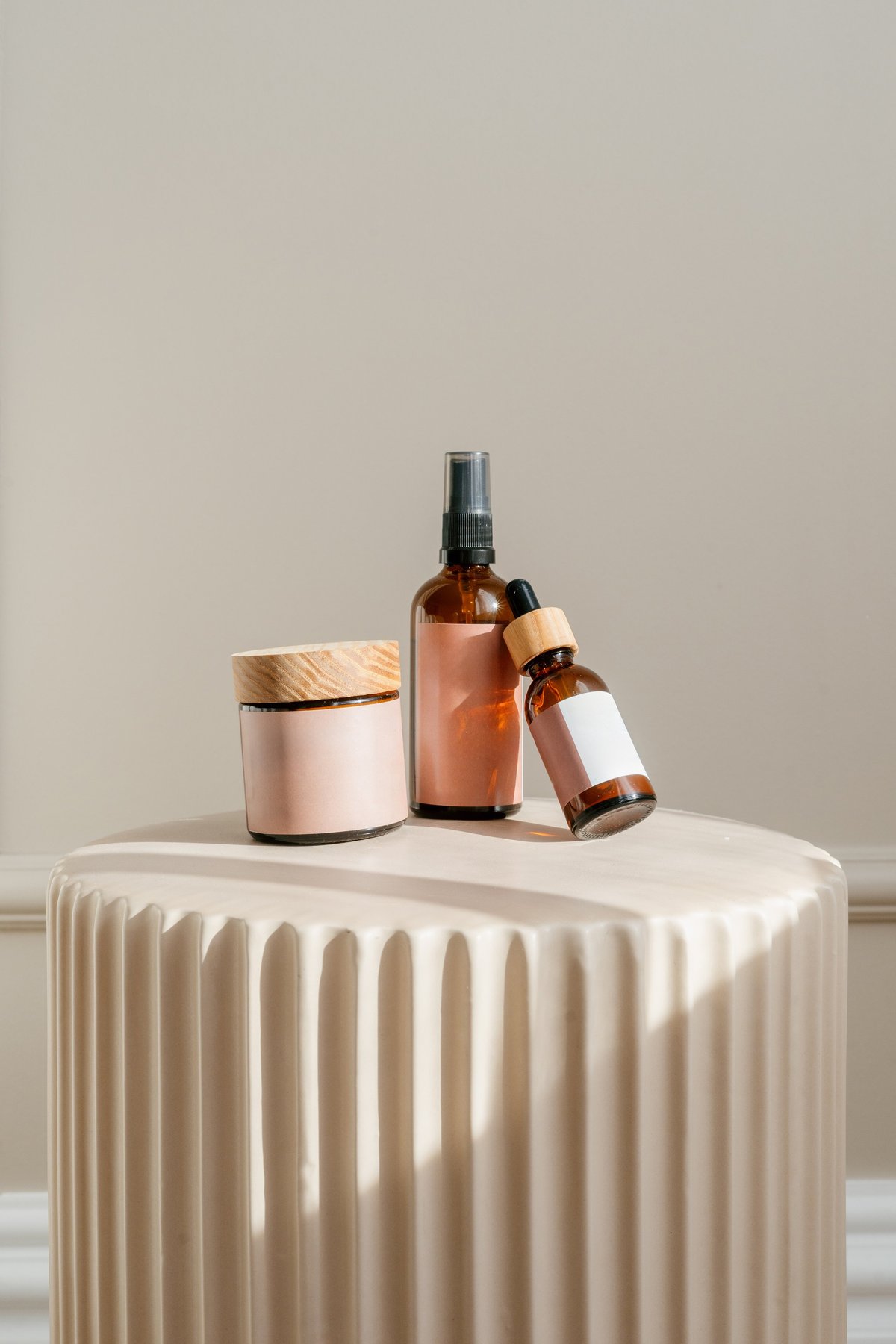 Vertical shot of beauty products, including a jar with face cream, spray bottle and dropper with anti wrinkle serum, rest on a stylish pedestal.