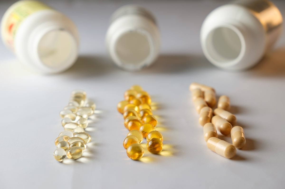 Various colored capsules and soft gels are laid out in a neat arrangement beside several opened supplement bottles. The setting suggests health-focused choices and wellness exploration.