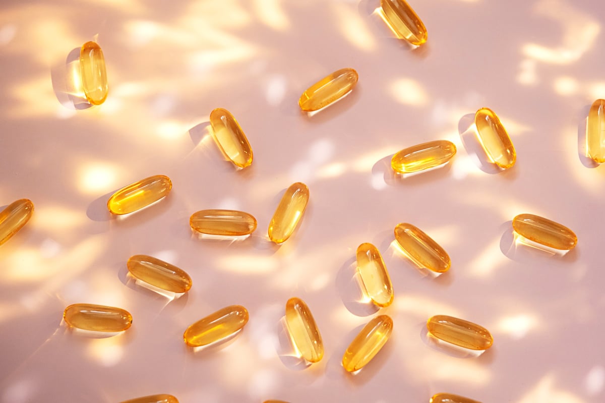 Yellow fish oil capsules on light pink background with sun glare and shadows. Health supplement for wellbeing and nutrient intake.