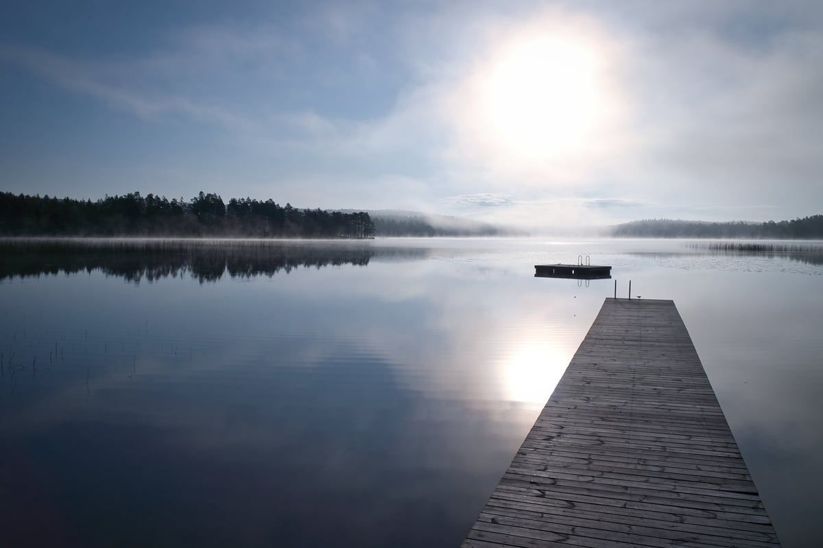 A wooden pier on a lake in the golden light of the sunset. The calm water surface, with rolling hills in the background, symbolizes peace, tranquility, and relaxation.