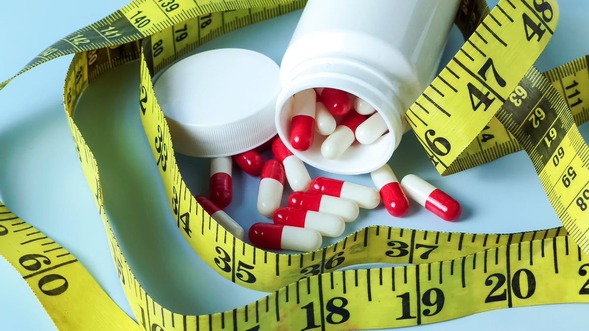 Spilled Diet Pills and a Yellow Measuring Tape Representing Weight Loss, Nutritional Supplements, and Health Goals