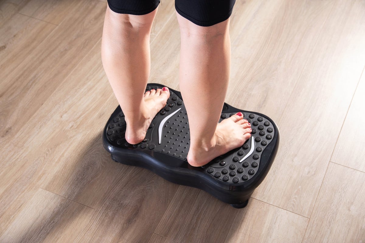 Women's legs stand on a sports vibration platform at home. Concept of doing sports at home. Modern home exercise machine