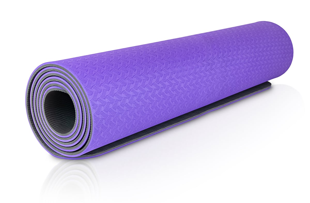 A rolled-up bright purple yoga mat with a textured pattern on a white background. The open edge reveals a black ribbed surface.