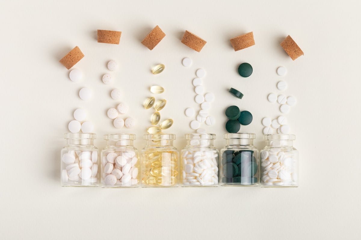 Small glass jars filled with vitamins, minerals, and food supplements from above on beige background