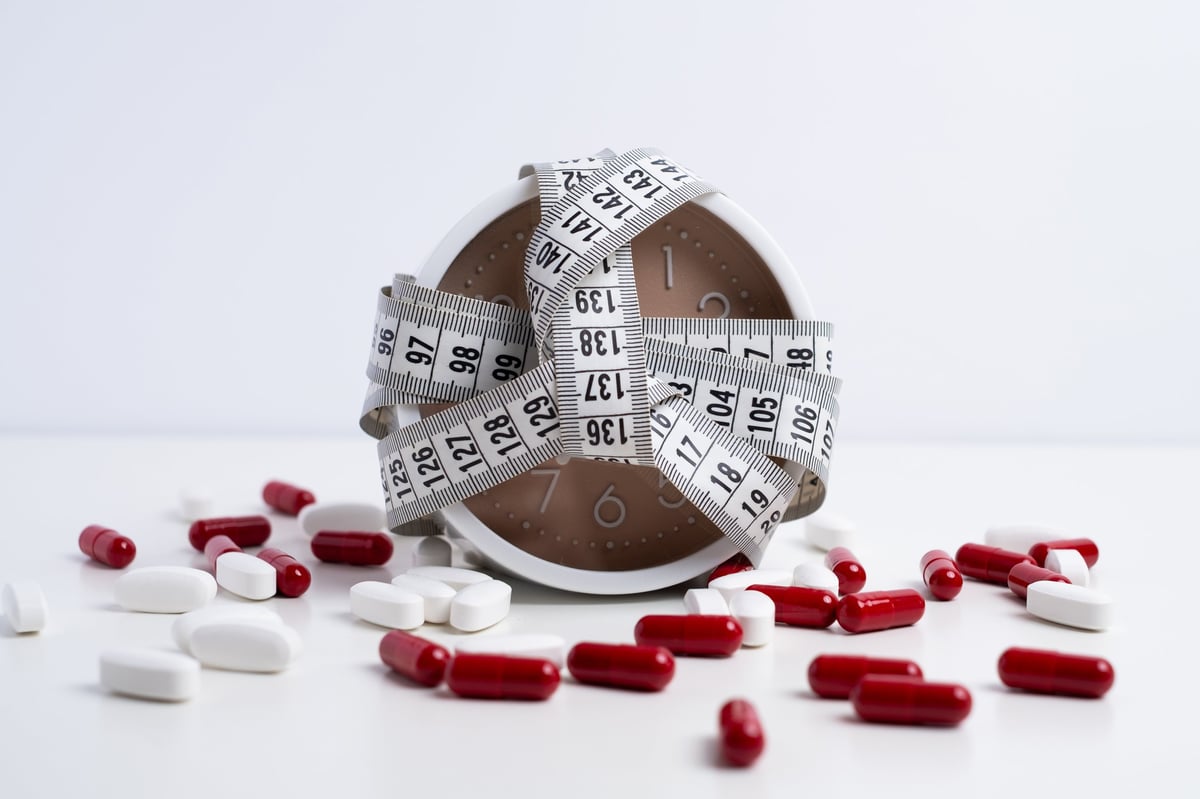 Alarm clock with measuring tape surrounded by red and white capsules. Weight loss and dietary supplement concept.