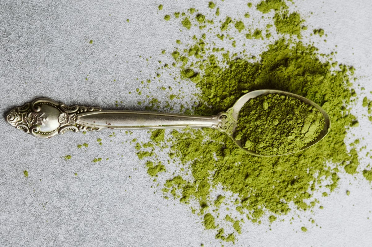 A silver spoon holds green powder on a gray surface.