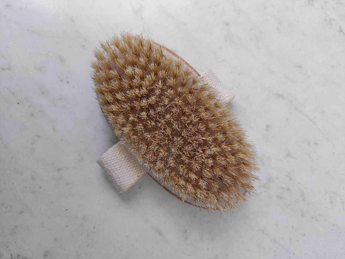 Close-up of a wooden massage body brush with natural stiff bristles and a fabric strap on a clean light surface. Perfect for anti-cellulite treatment, wellness, spa, and beauty care routines.